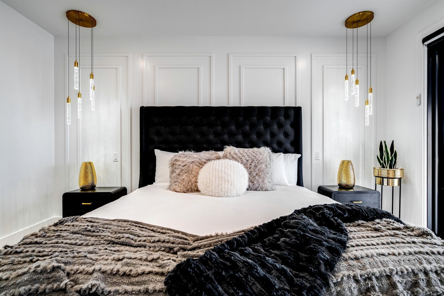 A modern bedroom with a black tufted headboard, white bedding, and a large black and white patterned throw.