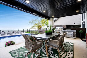A covered outdoor area with a pool, dining table, chairs, and a grill. - Sophisticated Shoreline Retreat with Sunset Patio & Poolside Lounging in Ontario, Canada (Leamington)