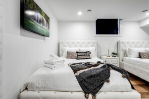 A modern bedroom with a large bed, two bedside tables, a flat-screen TV, and a painting of a waterfall. - Sophisticated Shoreline Retreat with Sunset Patio & Poolside Lounging in Ontario, Canada (Leamington)