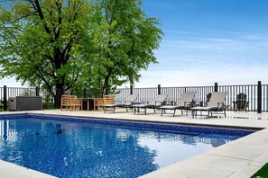 A swimming pool with lounge chairs and a wooden table, surrounded by a fence and trees. - Sophisticated Shoreline Retreat with Sunset Patio & Poolside Lounging in Ontario, Canada (Leamington)