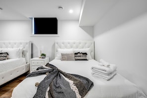 Une chambre moderne avec deux lits, une table de chevet et un téléviseur fixé au mur.