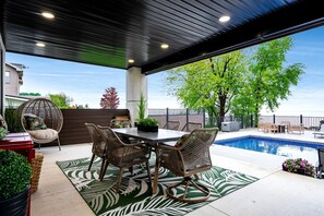 A covered outdoor area with a pool, wicker furniture, and a view of the sea. - Sophisticated Shoreline Retreat with Sunset Patio & Poolside Lounging in Ontario, Canada (Leamington)