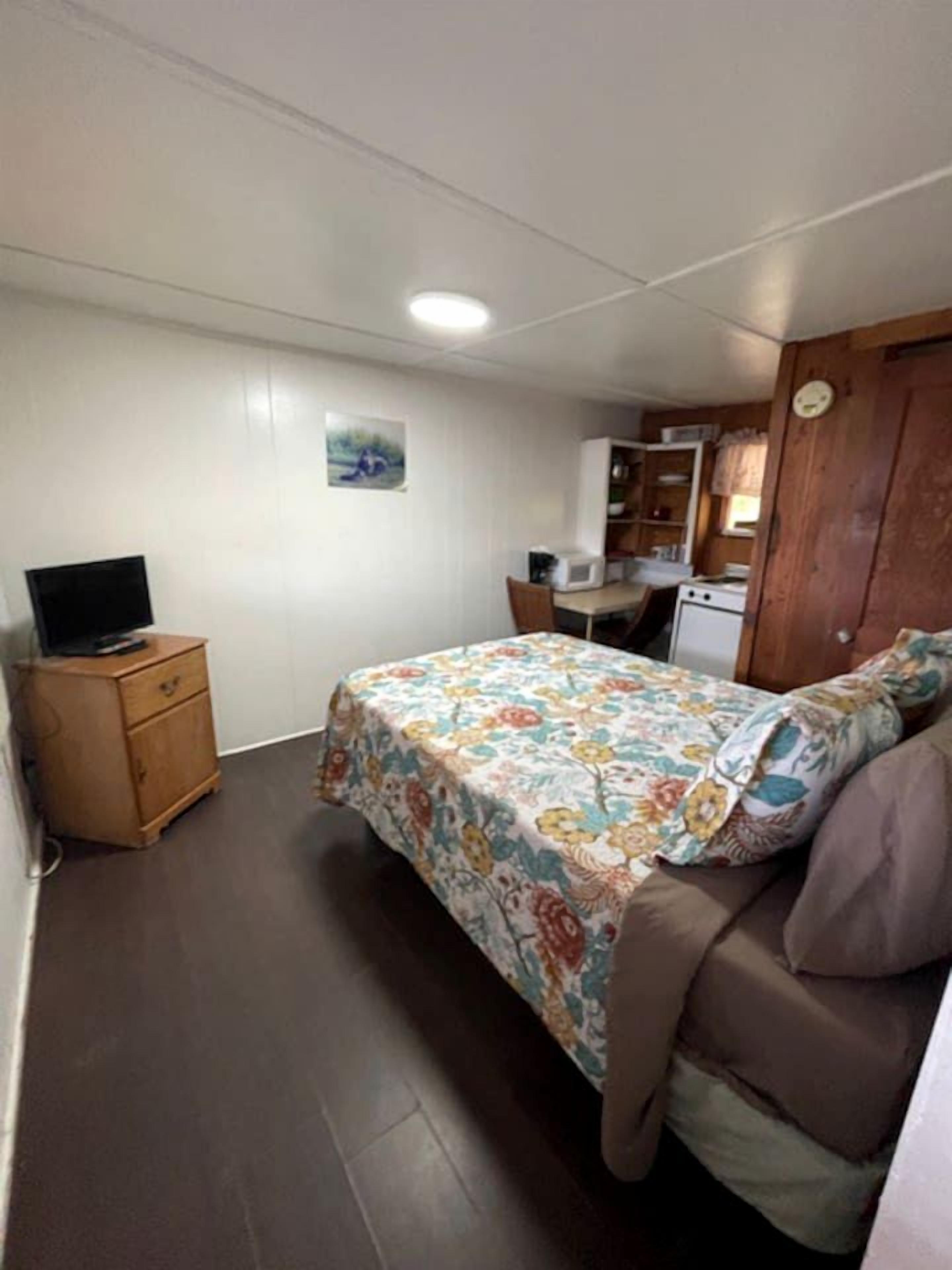 Una camera da letto con un letto, un comò in legno, una scrivania e un angolo cottura.