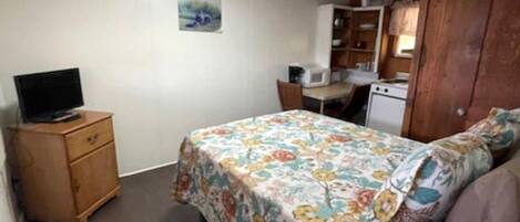 Een slaapkamer met een bed, een houten dressoir, een bureau en een kitchenette.