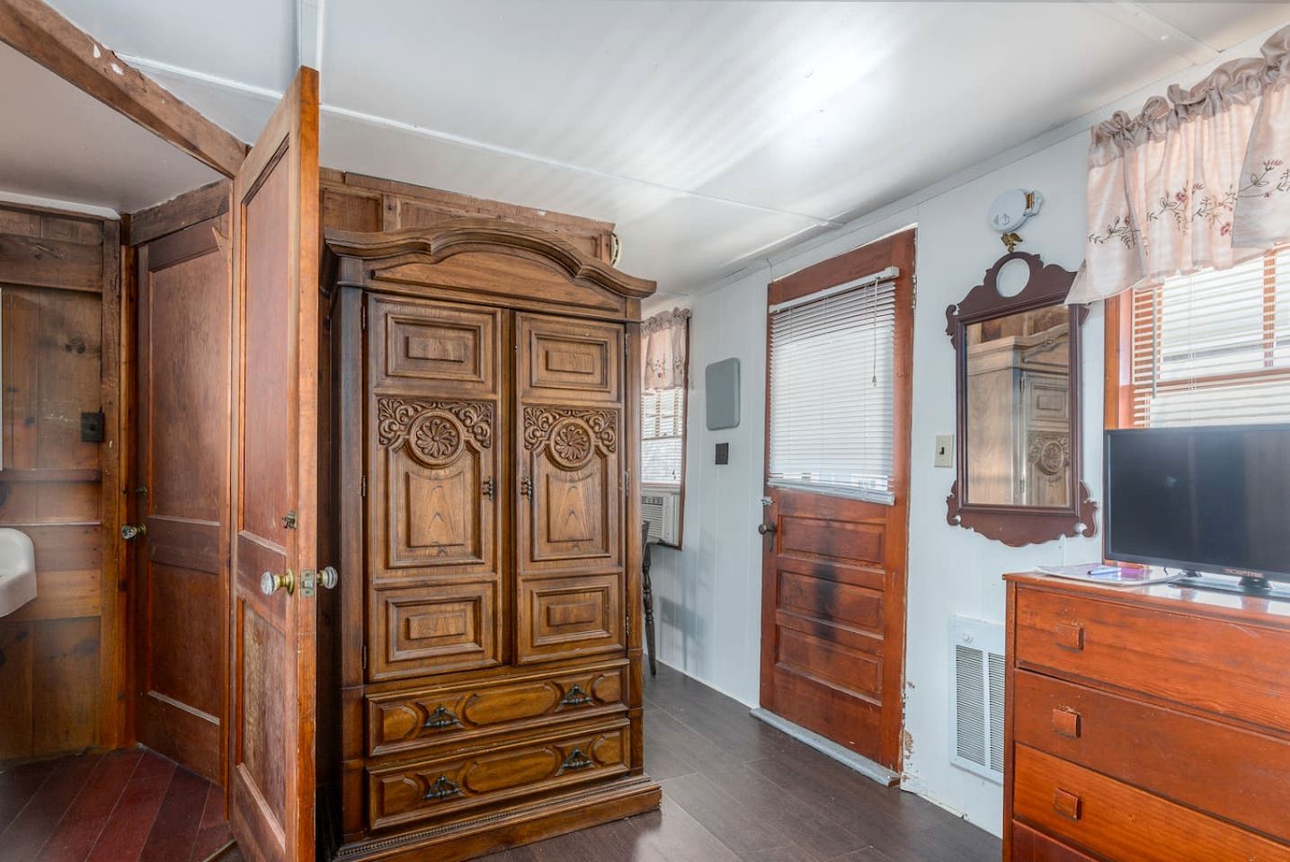 Une pièce avec une armoire en bois, un téléviseur et un miroir au mur.