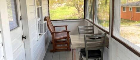 A covered porch with a wooden table and chairs, a door, and a view of a house.
