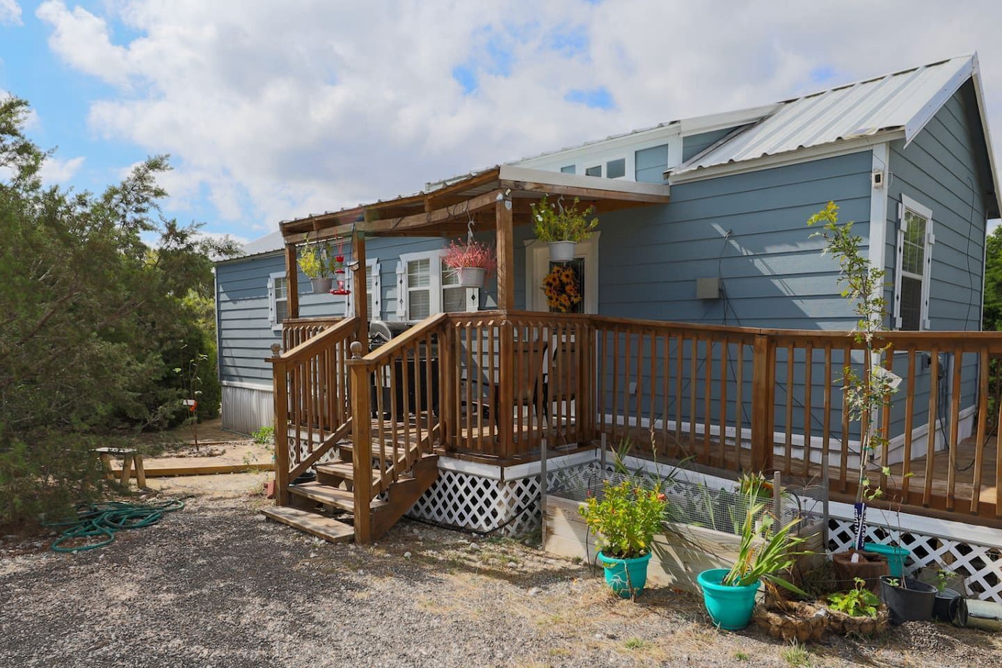 A single-story house with a wooden deck, a porch with a railing, and potted plants.