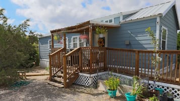 A single-story house with a wooden deck, a porch with a railing, and potted plants.