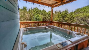 A hot tub under a wooden pergola with a view of trees.