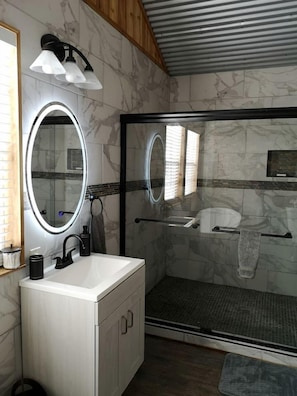 Un bagno con un mobile lavabo bianco, uno specchio grande, una cabina doccia in vetro e un porta asciugamani.