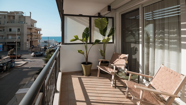 Uma varanda com vista para a rua, dois vasos de plantas e duas cadeiras de madeira.