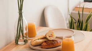 Uma mesa de madeira com um prato de comida, um copo de suco de laranja e um vaso com flores.