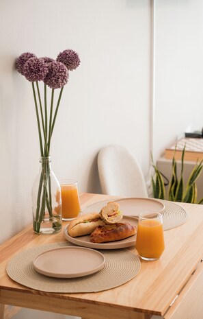 A wooden table with a plate of food, a glass of orange juice, and a vase with flowers. - ATOM – Minimal Luxury Stay in Rethymno with Parking & Self Check-in (Rethymno)