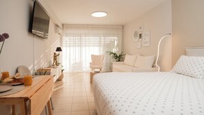 Quarto de hotel com cama, mesa de trabalho com café da manhã, uma cadeira, televisão e luminária.