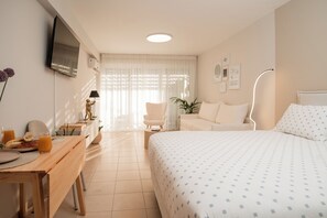 A hotel room with a bed, a desk with breakfast, a chair, a TV, and a lamp. - ATOM – Minimal Luxury Stay in Rethymno with Parking & Self Check-in (Rethymno)