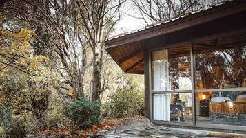 A rustic cabin with a stone foundation, large glass windows, and a wooden roof.