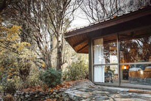 A rustic cabin with a stone foundation, large glass windows, and a wooden roof.