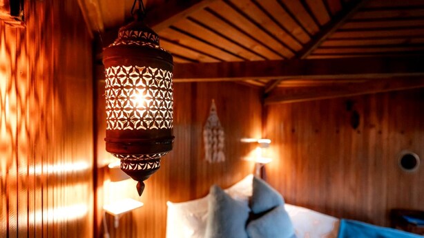 Une pièce en bois avec une lanterne suspendue, un lit avec des oreillers et une lampe fixée au mur.