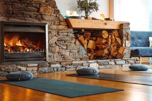 A stone fireplace with a fire, a stack of firewood, and yoga mats on the floor. - Magical Queenstown Cabin with Lake Views (Queenstown)