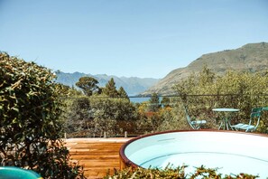 A pool with a wooden deck, a table and chairs, and a view of mountains and a lake.