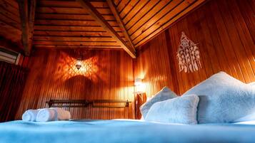 Ein Zimmer einer Holzjagdhuette mit einem Bett, Kissen, einer Wandleuchte und einem Wandbild.