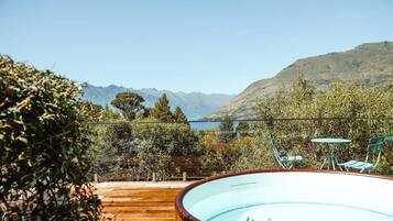 Une piscine entourée d’une terrasse en bois, avec une table et des chaises, et offrant une vue sur les montagnes et un lac.