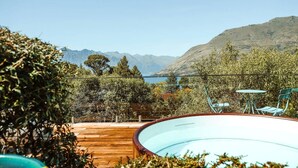 A pool with a wooden deck, a table and chairs, and a view of mountains and a lake.