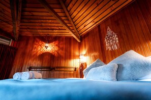 A wooden cabin room with a bed, pillows, a wall-mounted light, and a decorative wall hanging. - Magical Queenstown Cabin with Lake Views (Queenstown)