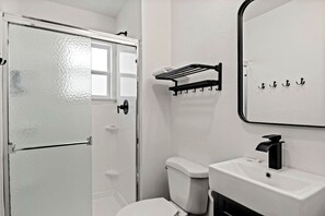 Ein Badezimmer mit Toilette, Waschbecken mit schwarzem Wasserhahn, Handtuchhalter und einer Duschkabine aus Glas.