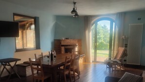 Ein Essbereich mit einem Holztisch und Stühlen, einem Kamin und Blick ins Freie durch eine Glastür.