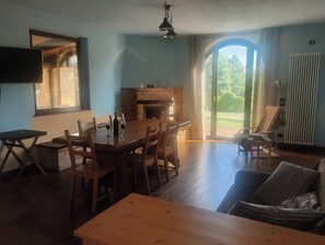 Ein Essbereich mit einem Holztisch und Stühlen, einem Kamin und Blick ins Freie durch eine Glastür.