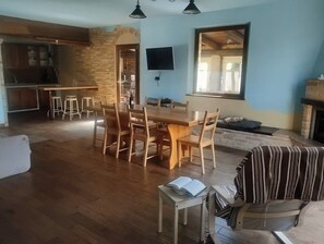 Ein geräumiger Wohnbereich mit Esstisch aus Holz, Barhocker, einer Couch und einem Kamin.
