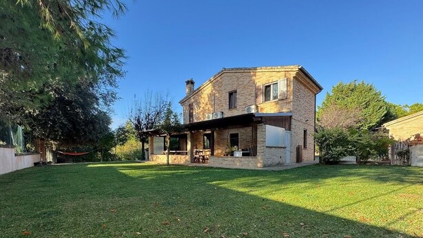 Ein zweistöckiges Haus mit einer überdachten Terrasse, einem Rasen und blauem Himmel.
