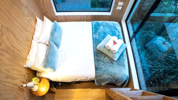 Ein gemütliches Schlafzimmer mit Oberlicht, einem Bett mit Kissen, einem Nachttisch mit Lampe und Blick ins Freie.