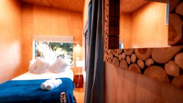 A wooden room with a bed, pillows, a bottle, and a window with a view.
