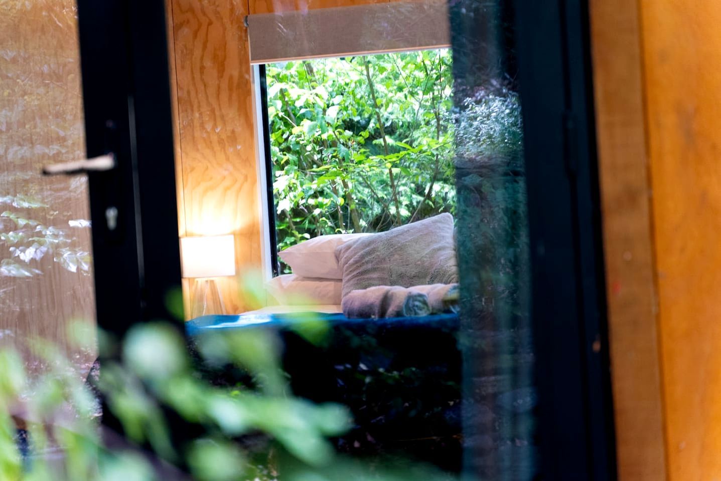 A bedroom with a bed, pillows, and a window overlooking greenery.