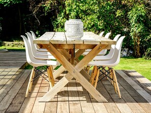 A wooden table with a glass centerpiece, surrounded by white chairs, set on a wooden deck.