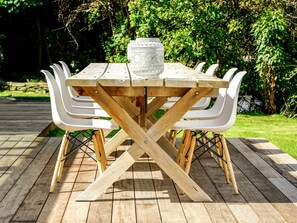 A wooden table with a glass centerpiece, surrounded by white chairs, set on a wooden deck. - Comfortable Cabin Rental for a Queenstown Holiday in New Zealand (Queenstown)