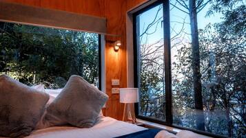 Une chambre avec une grande fenêtre, un lit avec des oreillers, une table de chevet et une lampe.