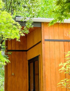 A wooden building with a door and window, surrounded by greenery.