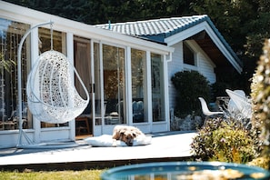 A house with a large glass door, a hanging chair, and a dog lying on a white pillow.
