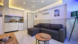 Un espacio habitable moderno con cocina, sofá, una mesa redonda de madera y una lámpara de pie.