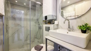 Un baño moderno con ducha de vidrio, un lavamanos blanco y un inodoro.