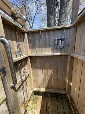 A wooden outdoor shower with metal fixtures and a bench.