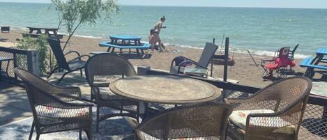 A beachside seating area with wicker chairs and a round table, overlooking the sea.