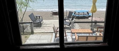 Quarto com uma grande janela para uma praia, com cadeiras de descanso e um guarda-sol amarelo.