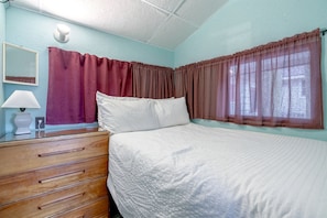 A bedroom with a bed, a dresser with drawers, a lamp, and curtains.