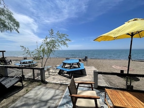 A beachside patio with tables and chairs, a yellow umbrella, and a view of the sea.