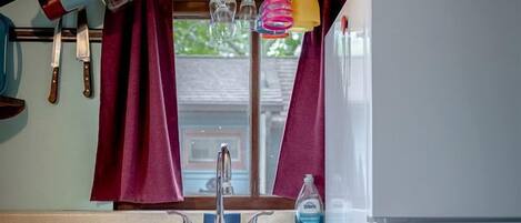 A compact kitchen with a sink, a refrigerator, and a window with curtains.