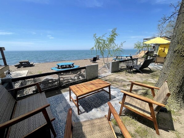 Un patio frente a la playa con mobiliario exterior, una mesa y vistas al océano.
